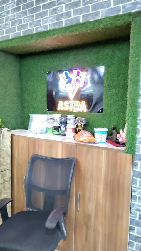 A reception nook with an artificial-grass surround, a lit "Astra" sign on the wall above a wooden cabinet, and an office chair.